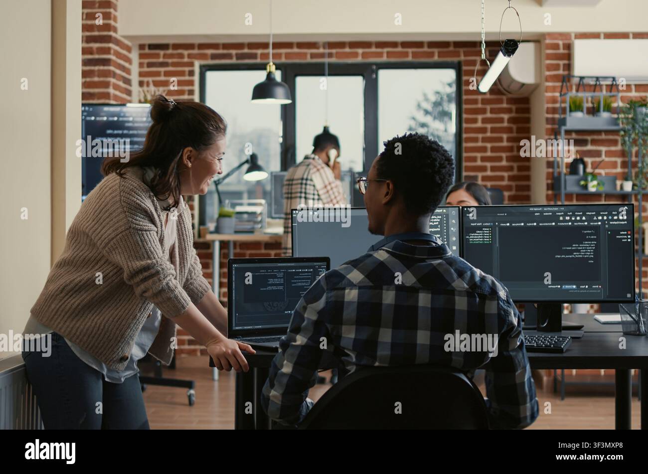 Two software developers doing high five hand gesture at desk with multiple screens running ai code celebrating successful algorithm, programmers colleagues enjoying teamwork results in it agency. Stock Photo