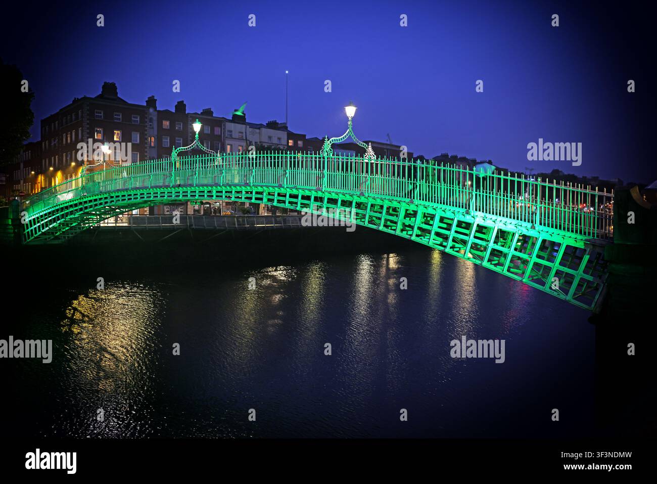 Green illuminated Ha'penny Bridge spans the River Liffey in Dublin city centre at romantic blue hour, reflected in the dark water,a great city break Stock Photo