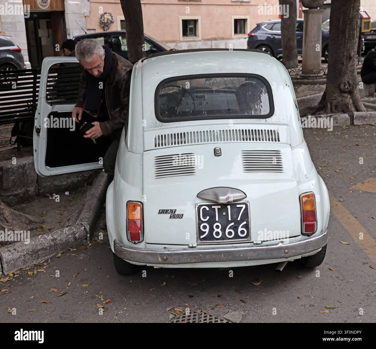 Classic white Fiat 500 car with a man loading the rear luggage compartment, photographed in Italy. Stock Photo