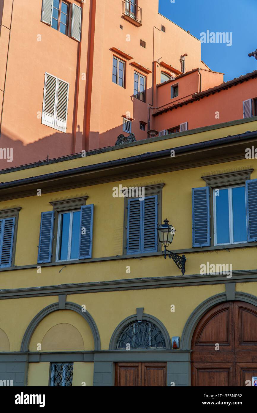 A charming view of historic Italian architecture featuring contrasting yellow and peach facades with traditional shutters, arched doorways, and elegan Stock Photo