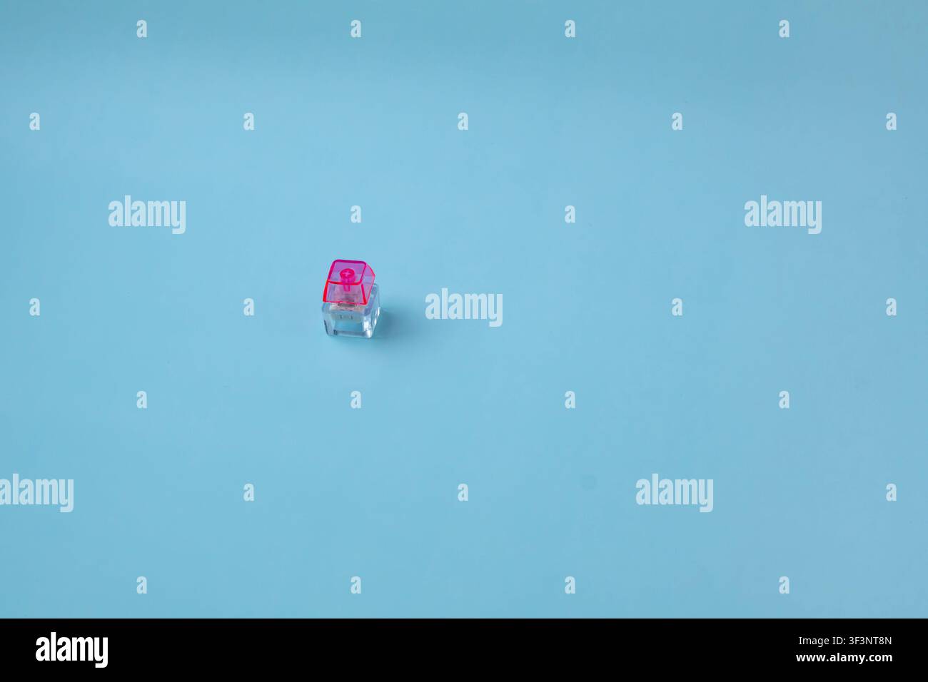 Single Transparent Mechanical Keyboard Switch with Pink Stem on Blue Background Stock Photo