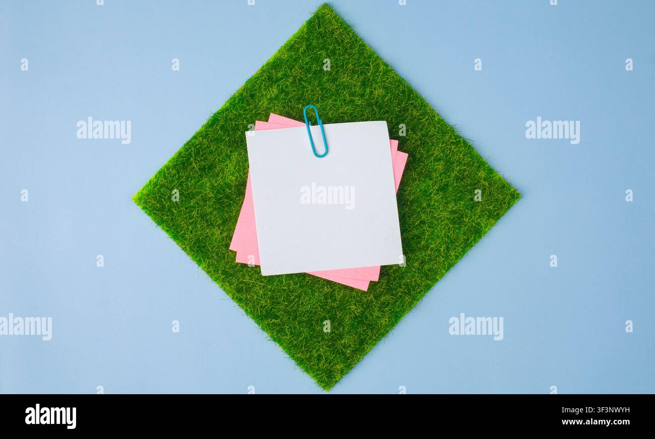 Sticky Notes on Square Grass Patch over Blue Background Stock Photo