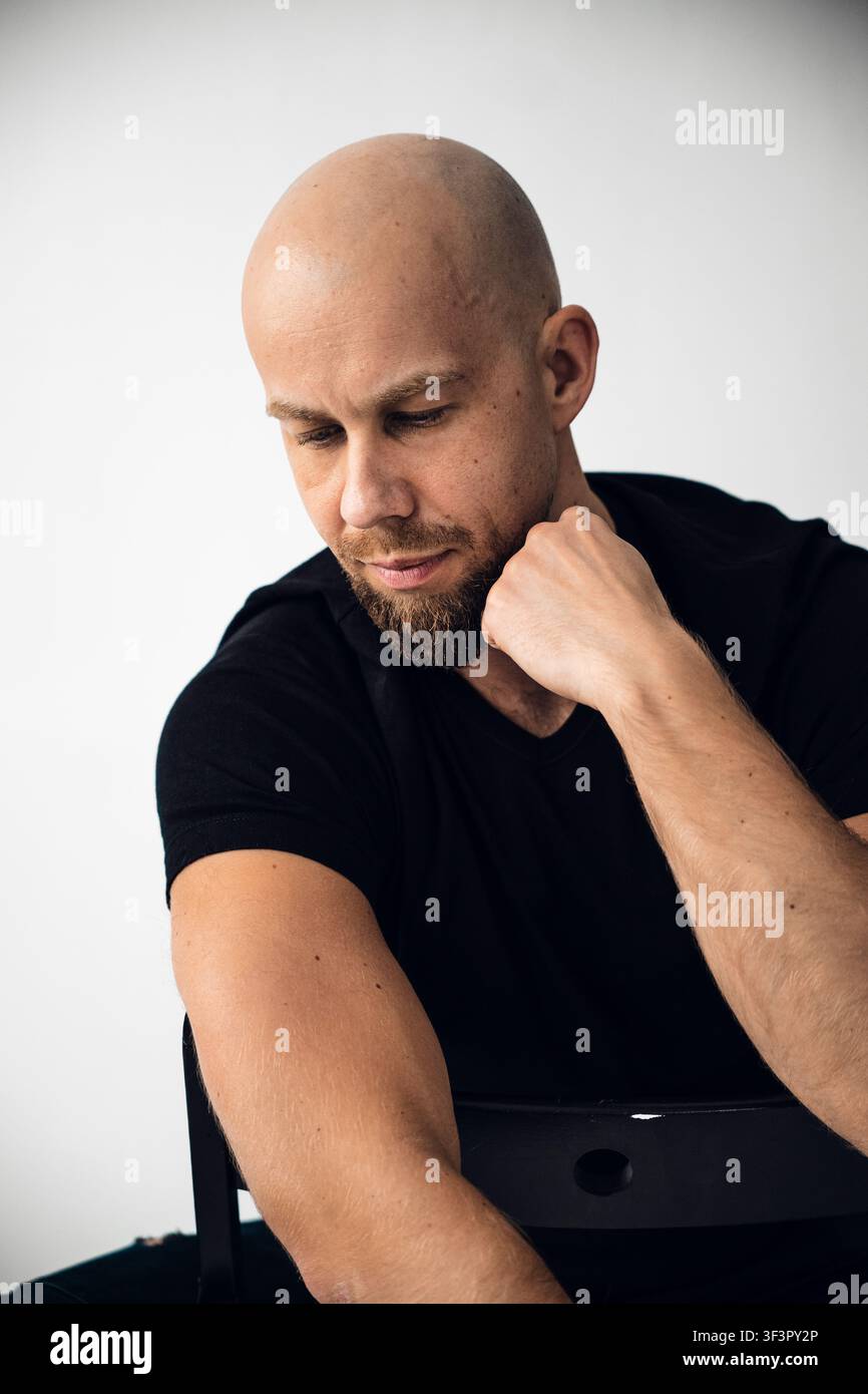 Man with a bald head and beard sits thoughtfully in a studio setting Stock Photo