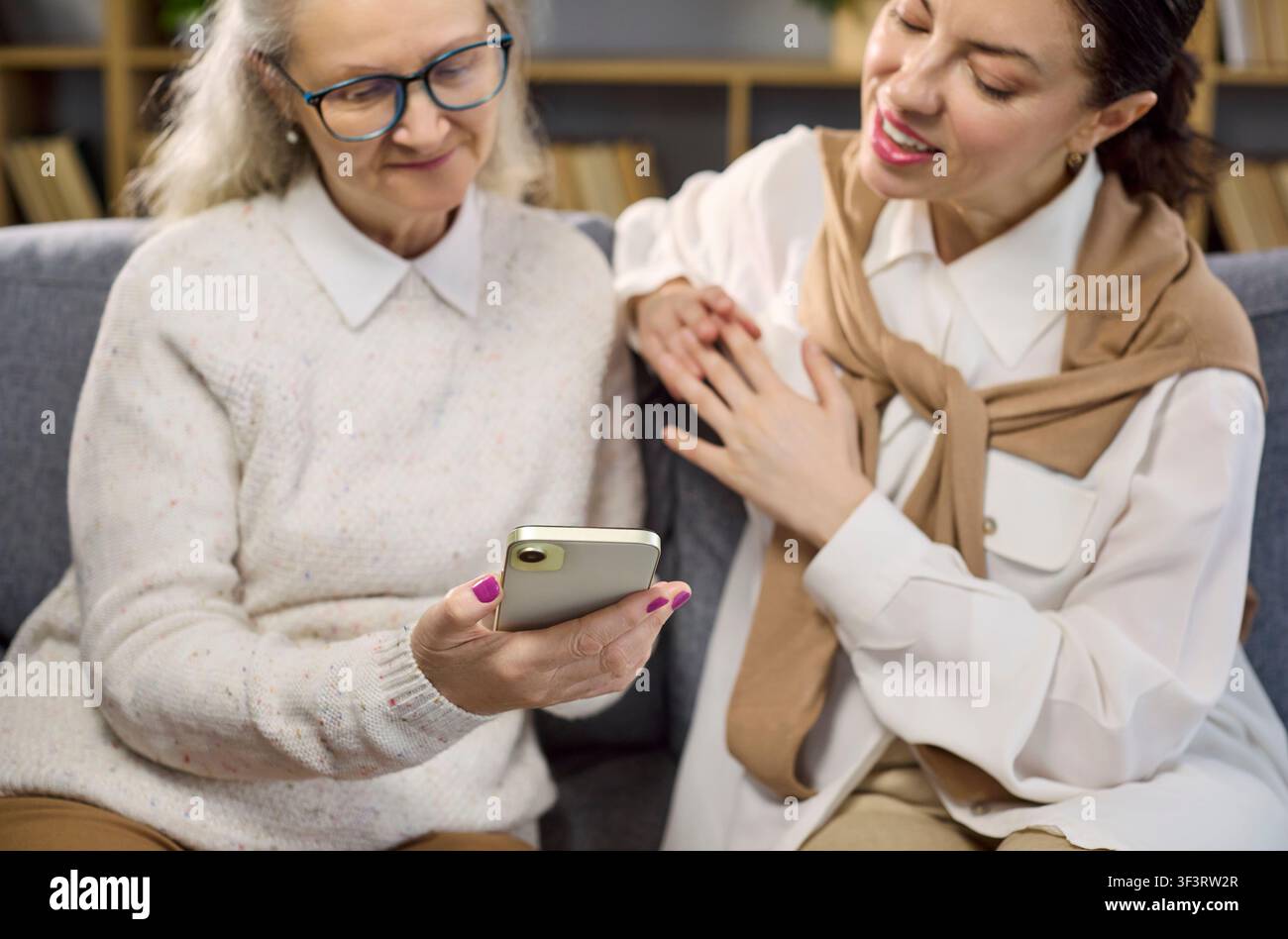 Daughter guides elderly mother using smartphone for online services and tasks Stock Photo