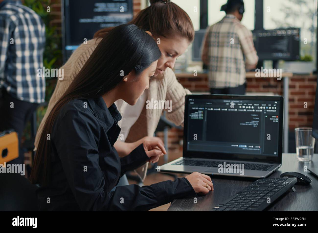 Software development team reviews laptop source code at a desk in a server room, collaborating on artificial intelligence, database work and a coding project. Stock Photo