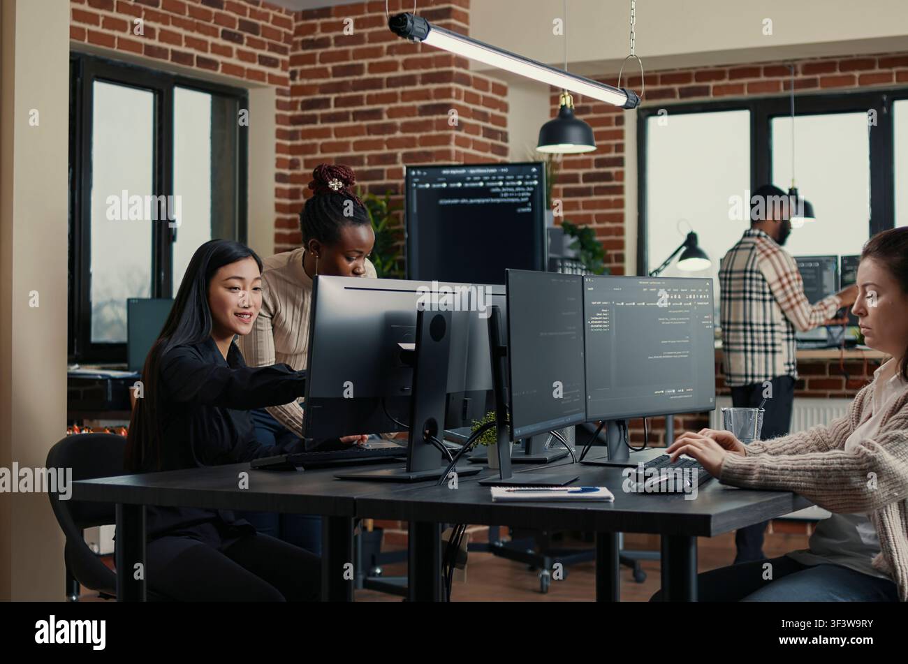 Software engineer types source code at a computer keyboard while colleagues join a group project in an IT startup office during a coding workflow. Stock Photo