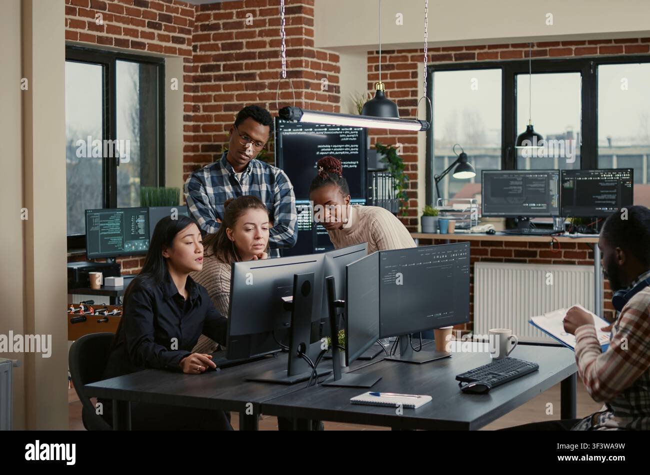 Software team discusses code feedback together while a developer team discusses algorithms, database work and new software ideas across office computer screens. Stock Photo