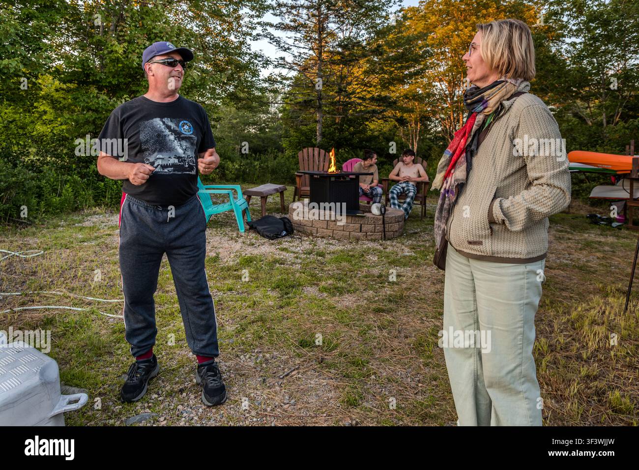 Timothy Doucette and Angela Berg on the grounds of the Deep Sky Eye Observatory on Frotten Road near Tusket, Nova Scotia, Canada. In the background, two teenagers are sitting by the fire as dusk falls – visitors gather here before the start of the nightly observatory tour Stock Photo