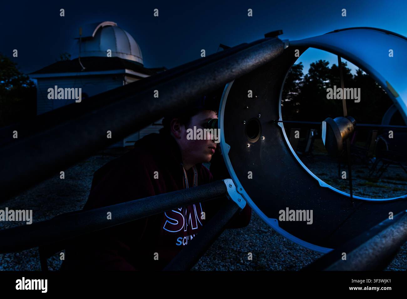 A junior researcher looks through the eyepiece of a large Dobsonian telescope on the grounds of the Deep Sky Eye Observatory on Frotten Road in the Municipality of Argyle, Nova Scotia, Canada. The dome of the main observatory can be seen in the background Stock Photo