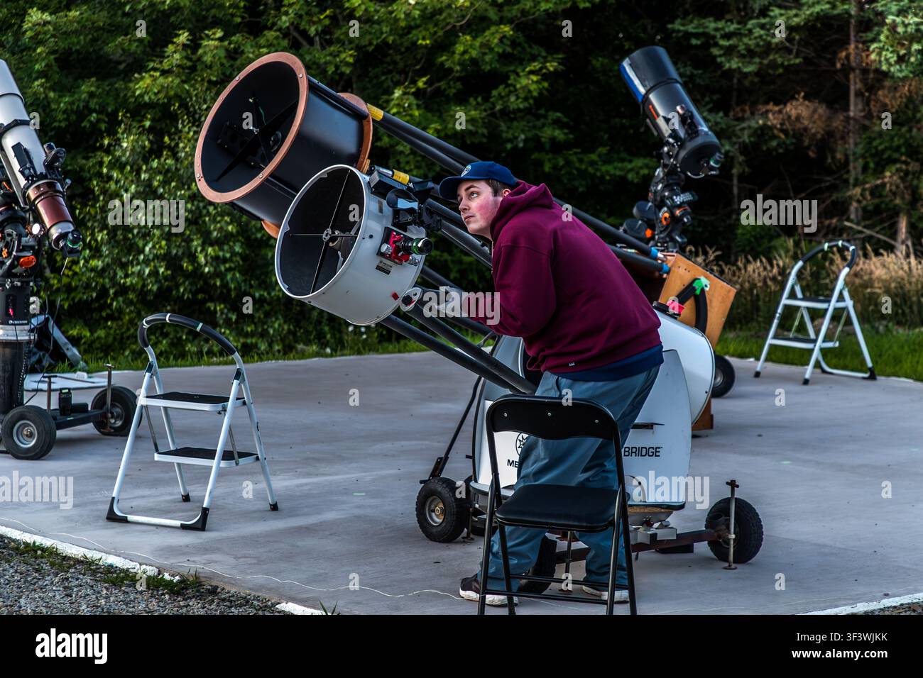 A young man is adjusting a telescope on the forecourt of the Deep Sky Eye Observatory on Frotten Road near Tusket, Nova Scotia. The observatory, which has been in operation since 2015, is situated in North America’s first Starlight-certified destination. Argyle Municipal, Nova Scotia, Canada Stock Photo