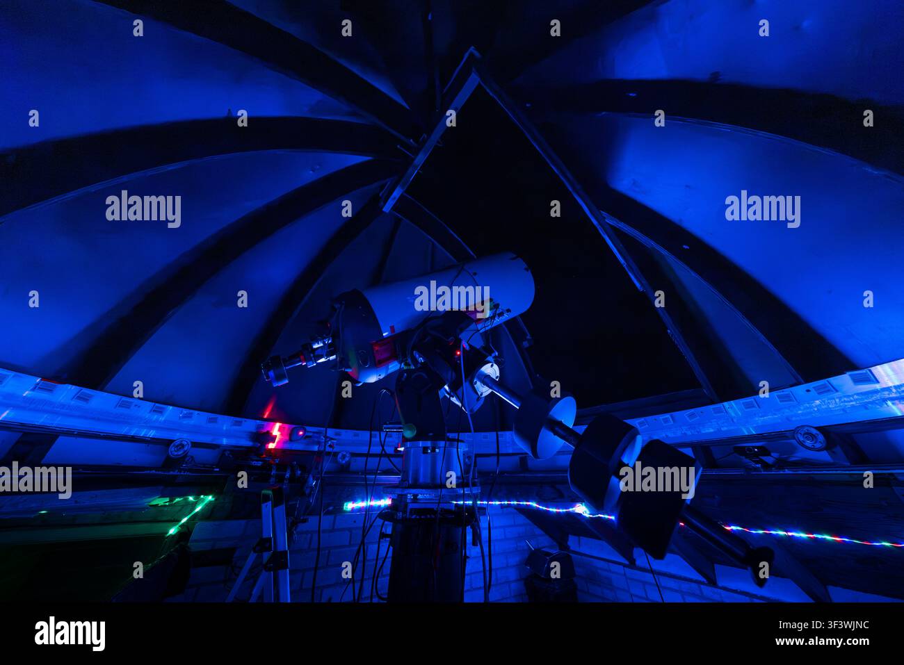 A computer-controlled telescope stands beneath the open dome of the Deep Sky Eye Observatory on Frotten Road in the Municipality of Argyle, Nova Scotia, Canada. Blue lighting is used during night-time operations to protect visitors’ night vision whilst the dome segments are open for observation. Argyle Municipal, Nova Scotia, Canada Stock Photo