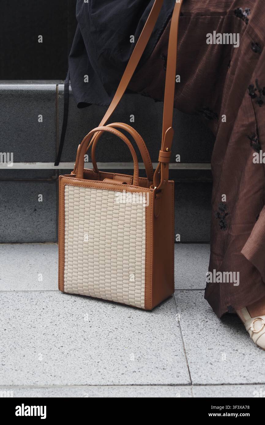 Small handbag sits on a floor near a person's leg Stock Photo
