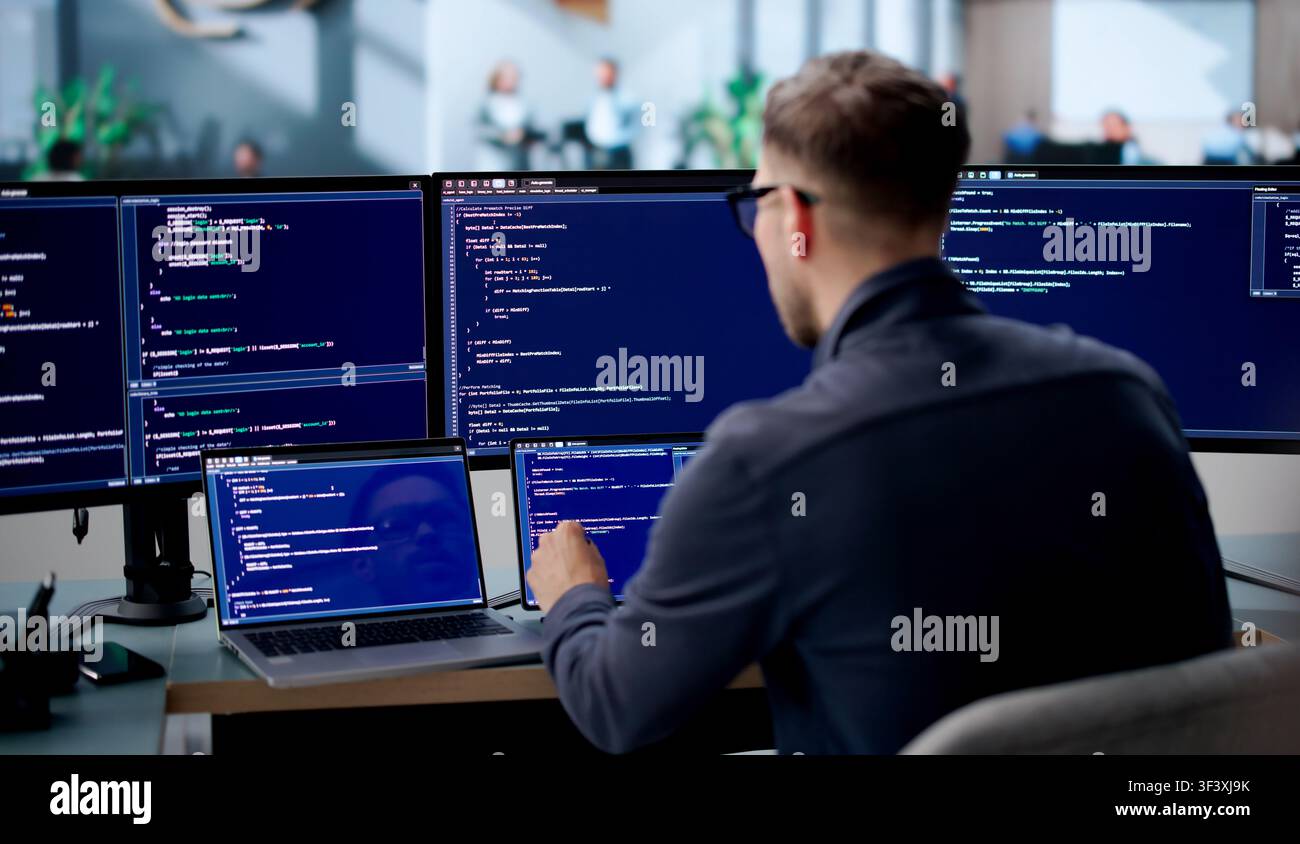 Young Male Software Engineer Coding Secure Algorithms On Laptop In Office. Stock Photo