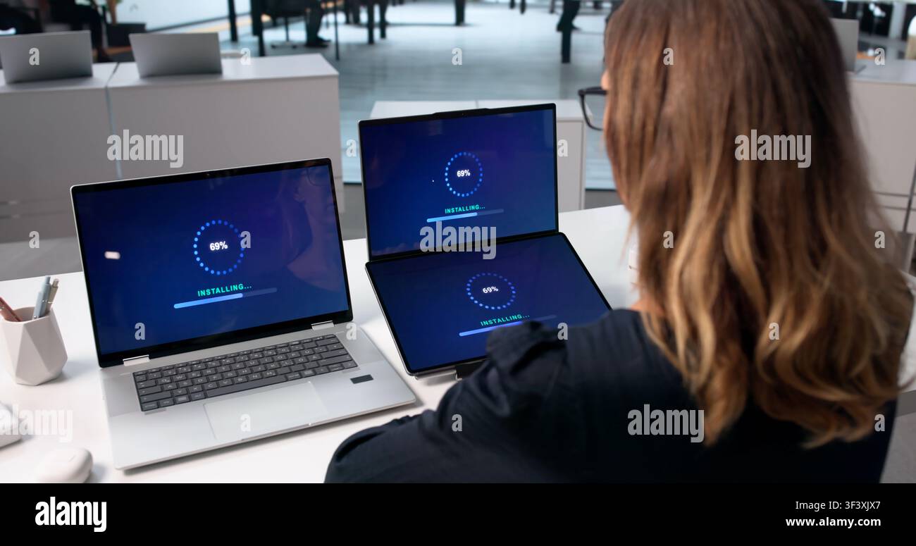 Woman Using Laptop To Install New Software Update On Touchscreen Device. Stock Photo