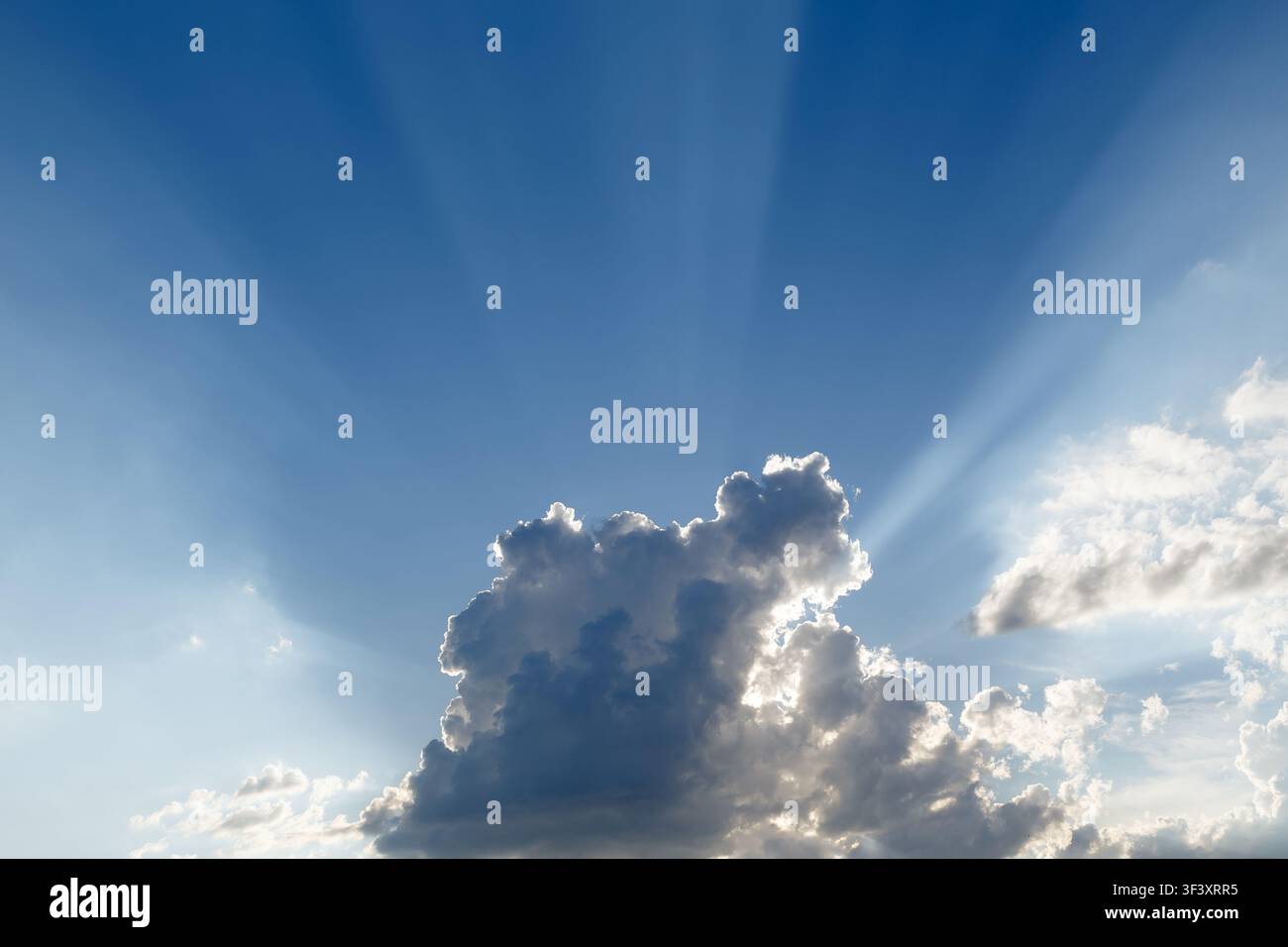 Dramatic blue sky with sun rays shining through fluffy white clouds Stock Photo