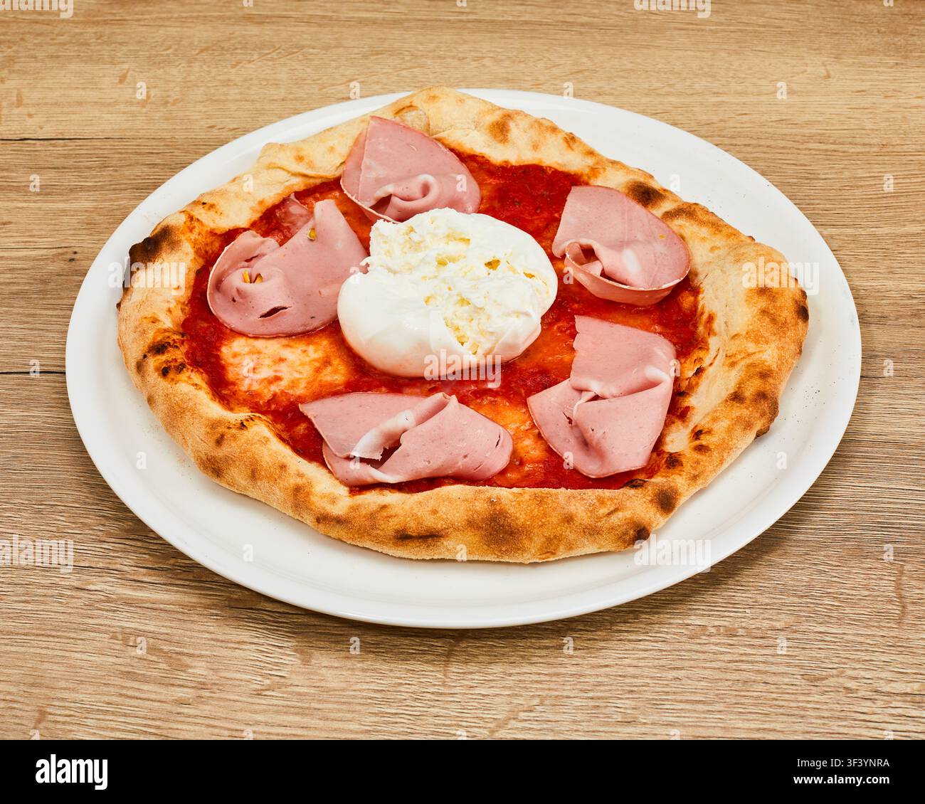 Whole Italian pizza with fresh burrata cheese, mortadella slices, and tomato sauce on white round plate on wooden tabletop. Stock Photo