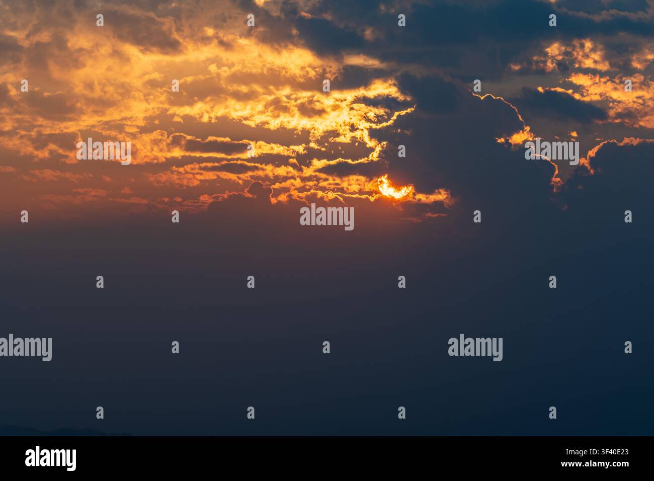 Dramatic sunset with sun partially hidden behind clouds and glowing sky. Stock Photo