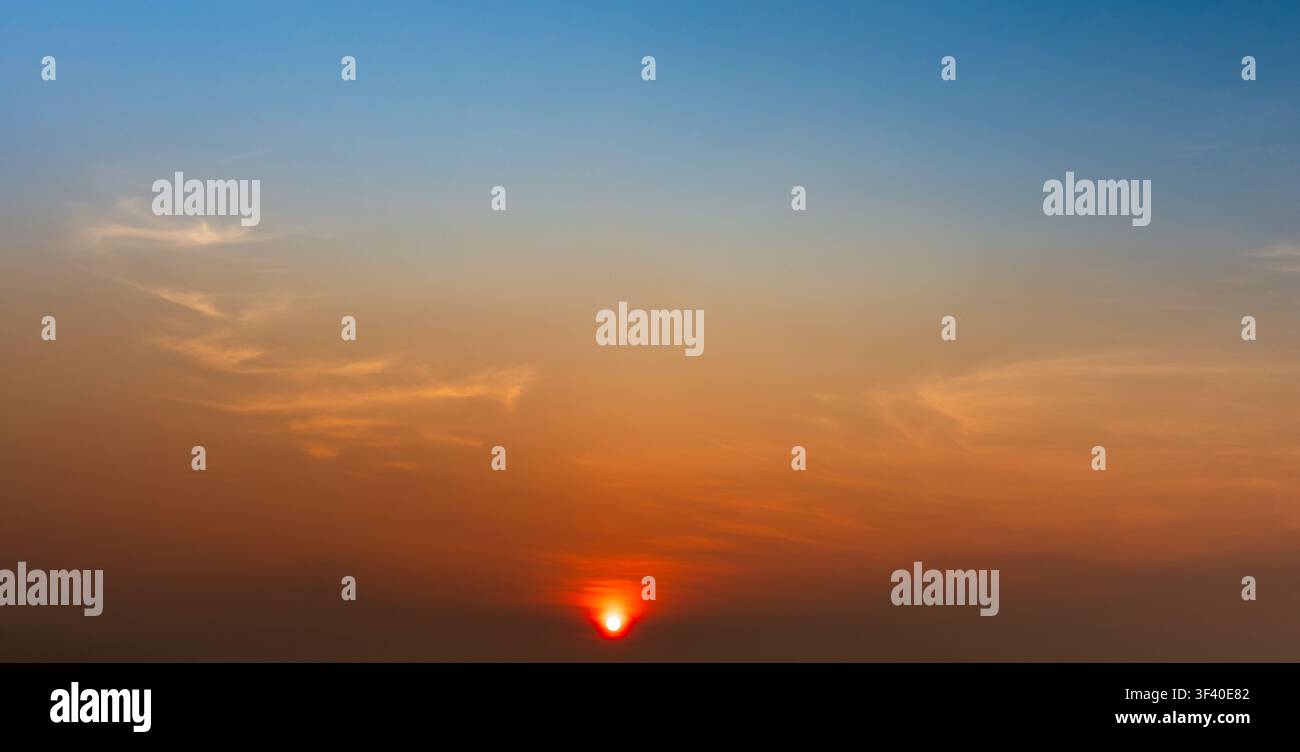 Bright orange sunset with blue gradient sky and soft clouds. Stock Photo
