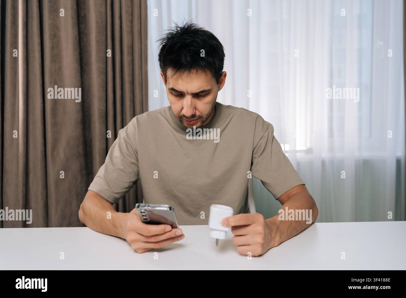 Portrait of man connecting smart home device using smartphone, looking at application settings, setting up and controlling smart socket from mobile ap Stock Photo
