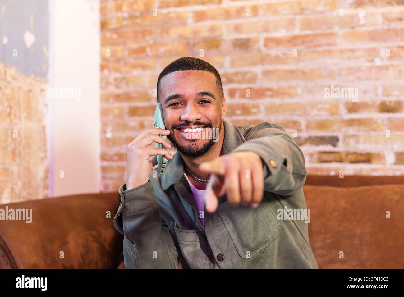 Smiling young man pointing finger while talking on phone Stock Photo
