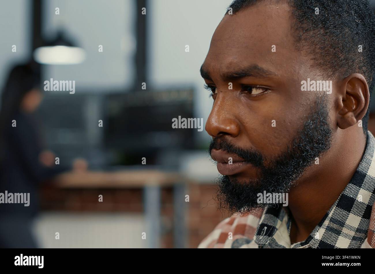 African American software developer types code while looking at a computer screen, with colleagues programming in the background in a software agency workflow. Stock Photo