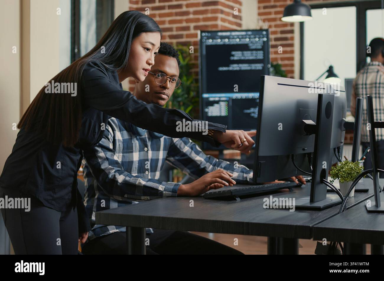 Two programmers carry a laptop with a coding interface toward a desk, preparing to discuss cloud computing and algorithm work with teammates. Stock Photo