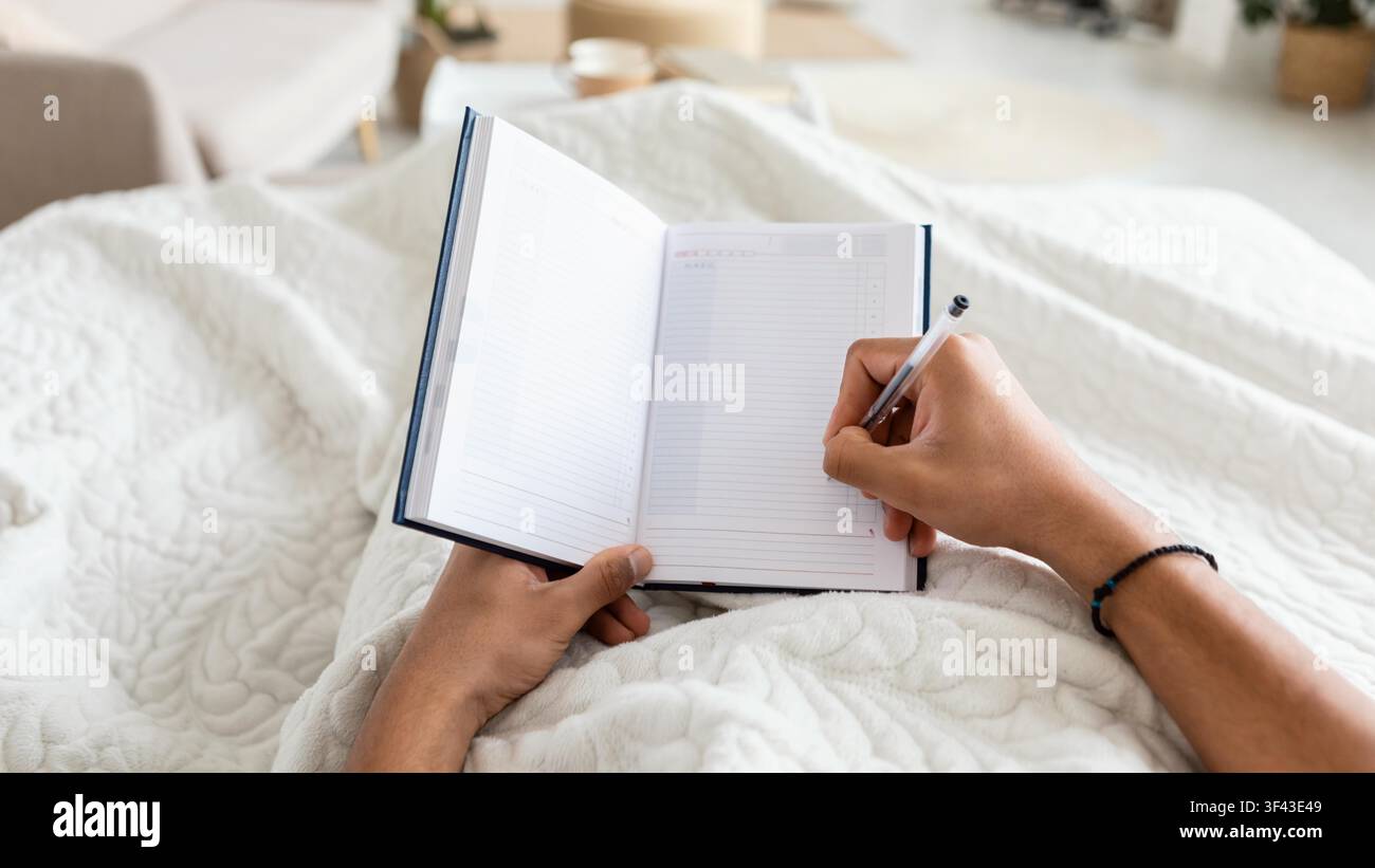Unrecognizable Person Writing In Notebook While Sitting Comfortable On Bed At Home Stock Photo