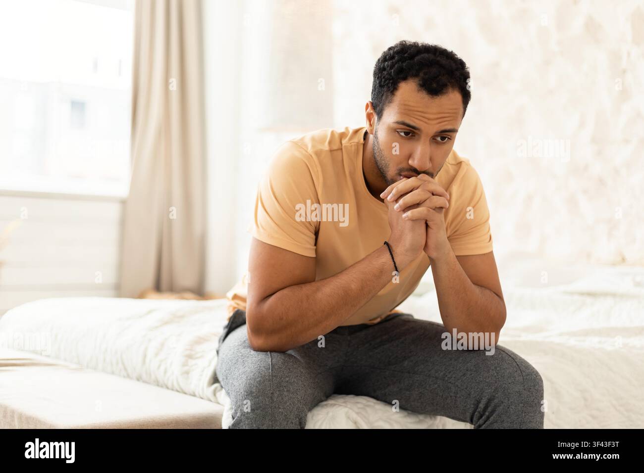 Worried Young Black Man Sitting On Bed In Bedroom, Deep In Thought, Mental Health Concept Stock Photo