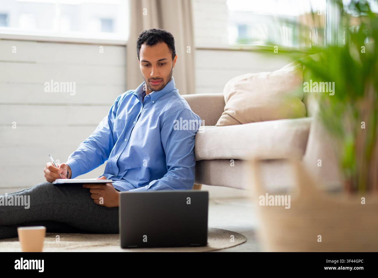 Focused Hispanic Male Student Taking Notes While Using Laptop On Floor At Home, Study Concept Stock Photo