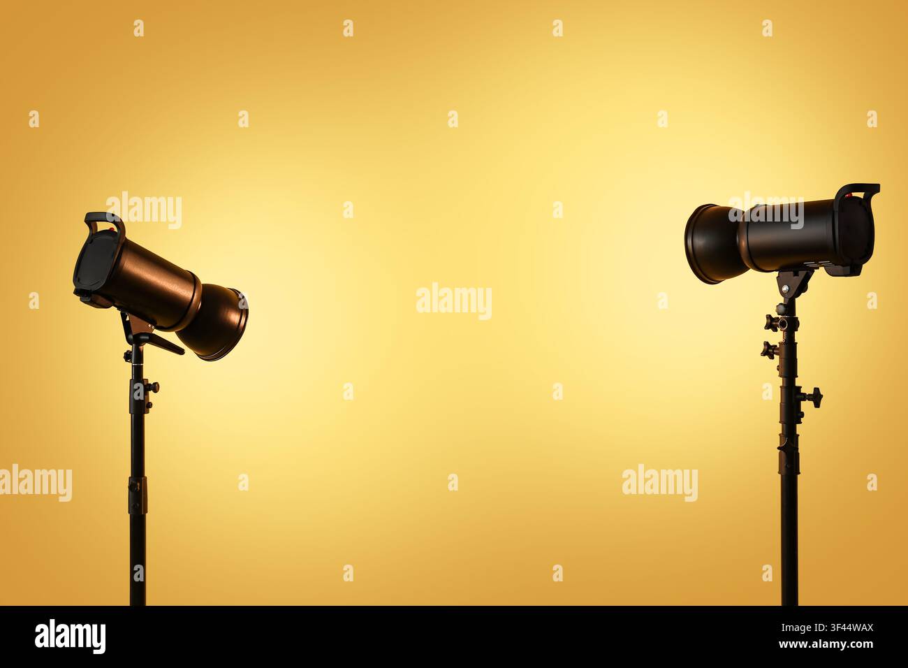 Two studio strobe lights on stands illuminating a warm yellow gradient background with copy space Stock Photo