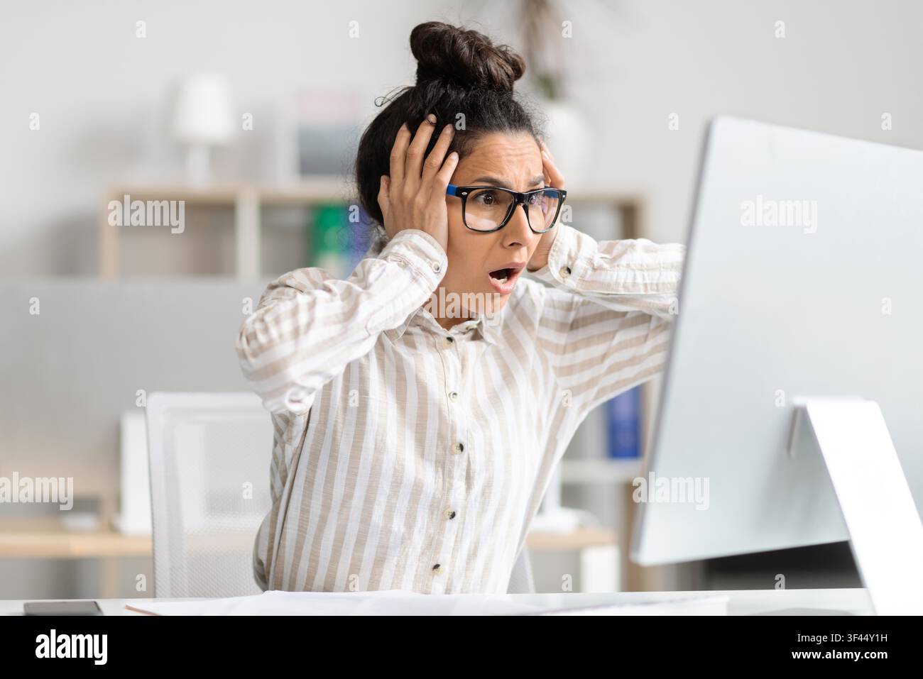 Worried Hispanic Female Office Worker Experiencing Stress While Working On Computer At Desk Stock Photo