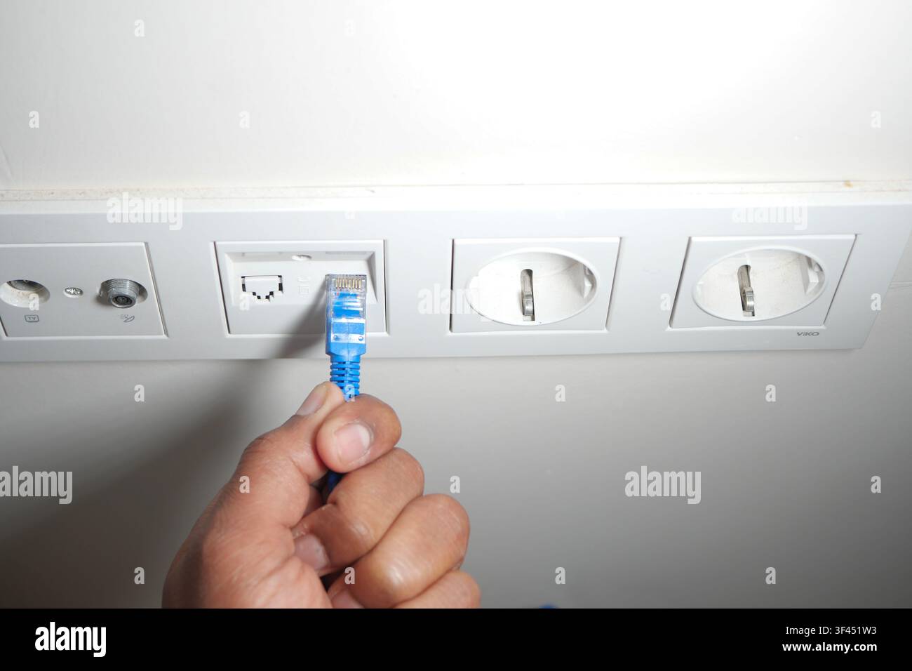 Connecting a blue ethernet cable to a wall socket Stock Photo