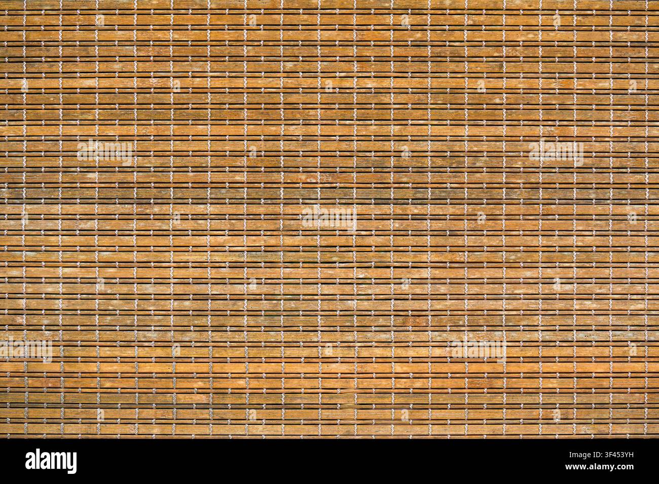Close-up of a natural bamboo mat or blind, featuring horizontal light brown wooden slats intricately woven together with contrasting white threads. A Stock Photo