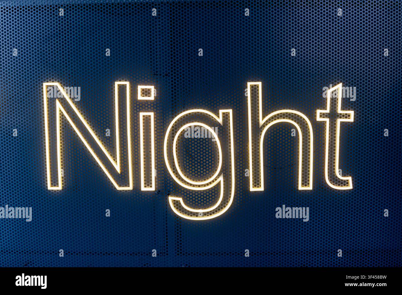 Night word illuminating a dark perforated metal background, signifying evening or leisure Stock Photo
