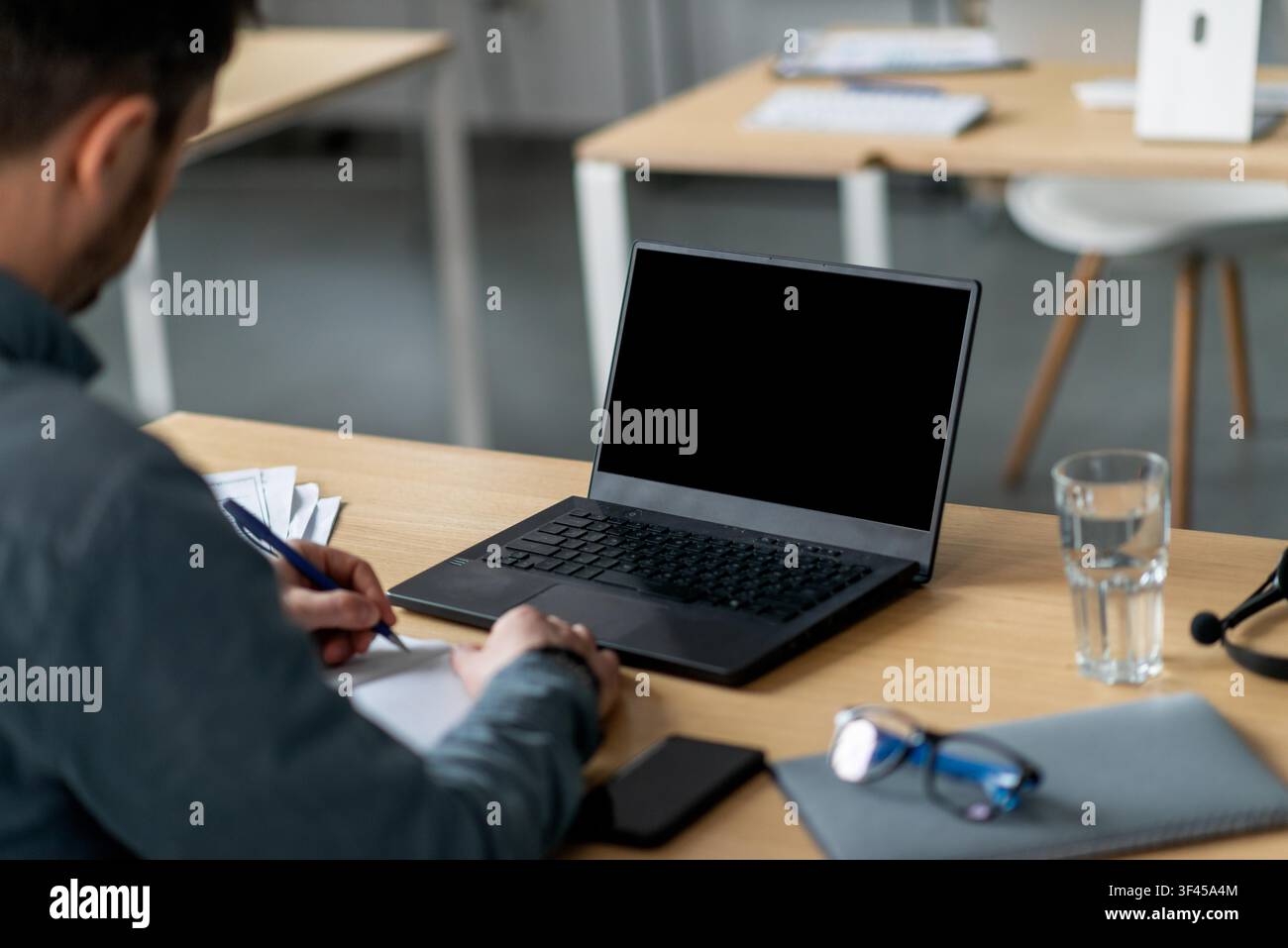 Unrecognizable Man Taking Notes On Laptop In Office Setting, Focused On Work Concept Stock Photo