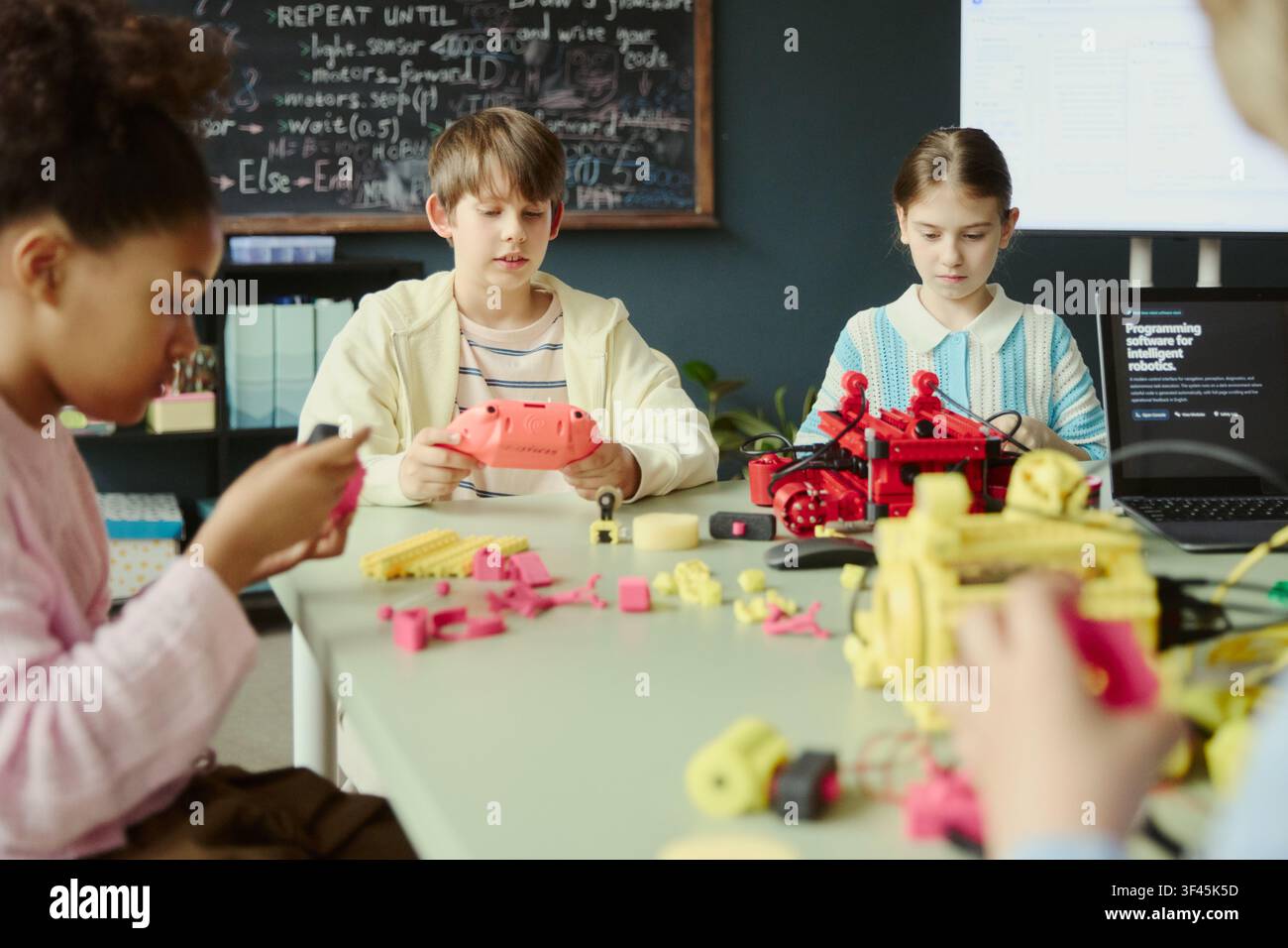 Multiethnic children assembling robotics models and testing controller during coding class, developing STEM teamwork skills. Ideal for education technology, makerspace, innovation marketing Stock Photo