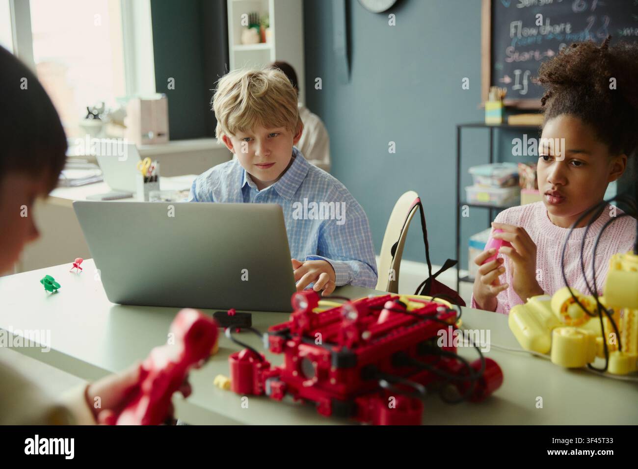 Diverse kids learning coding and robotics with laptop in classroom, building STEM teamwork and problem solving skills. Useful for education technology, STEM programs, digital learning Stock Photo