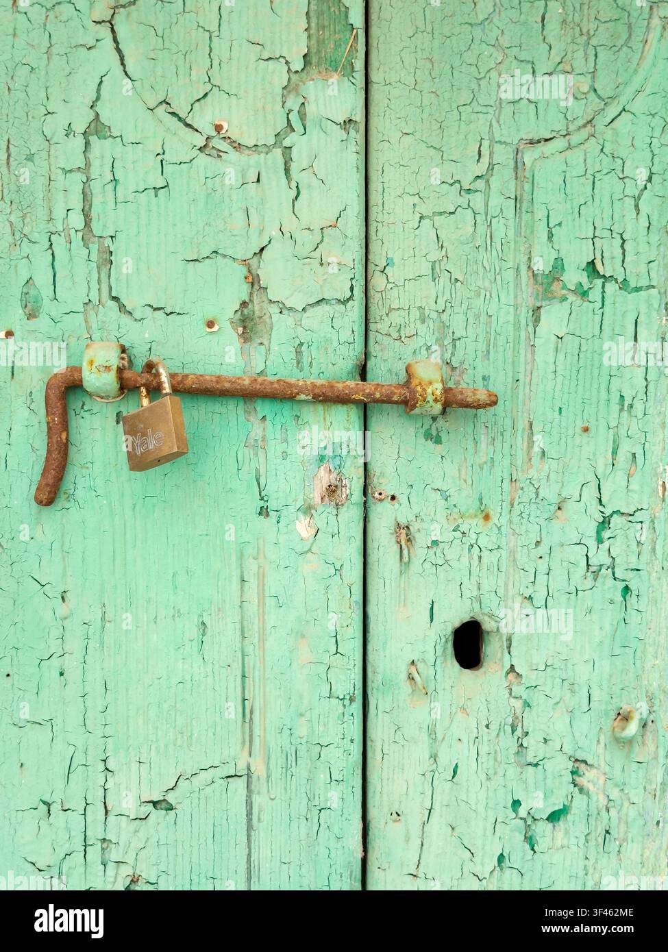 Weathered Door with a metal bolt and padlock, green peeling paint, in the town of Pisticci Stock Photo