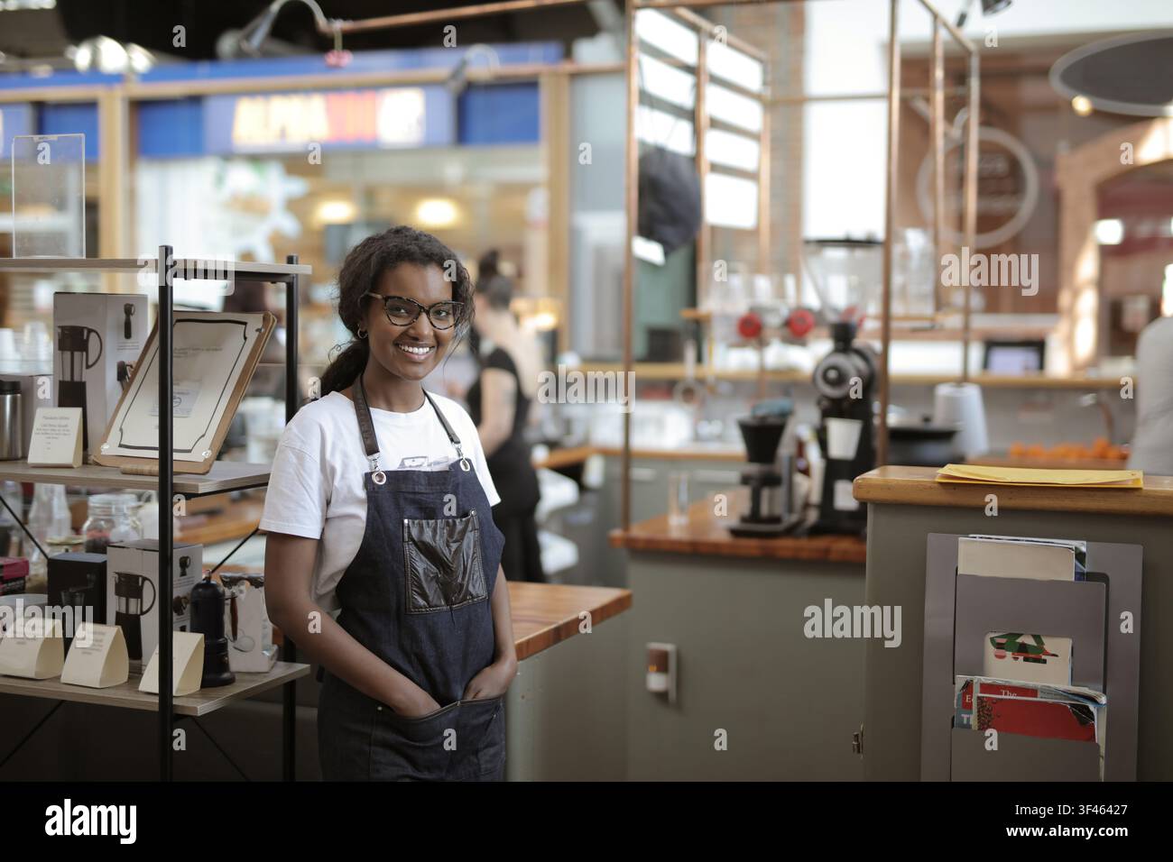 Friendly young barista smiling in her modern coffee shop Stock Photo