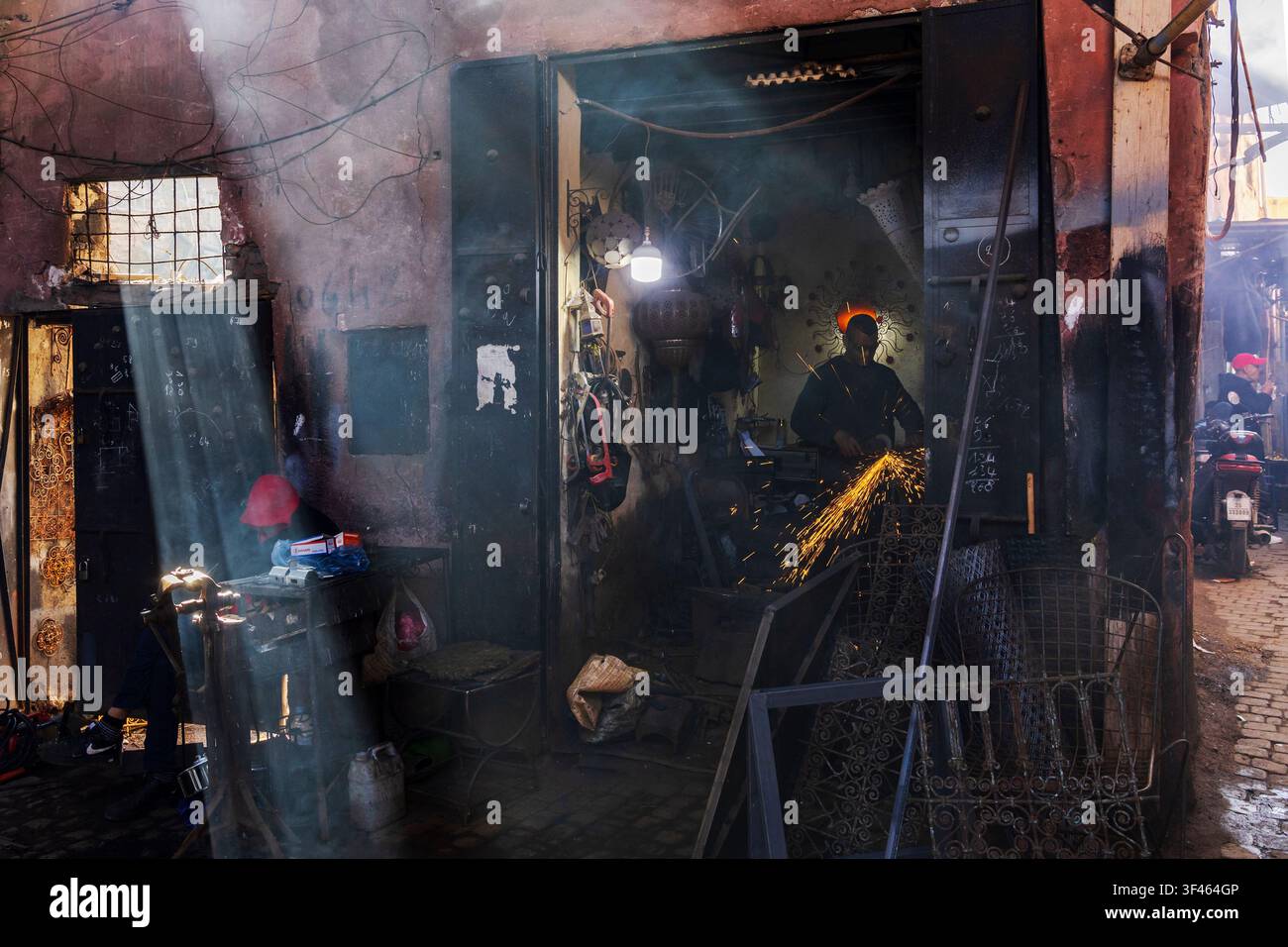 A small metalwork workshop in a souk, a man using a grinder creating sparks, light filtering through small window. Stock Photo