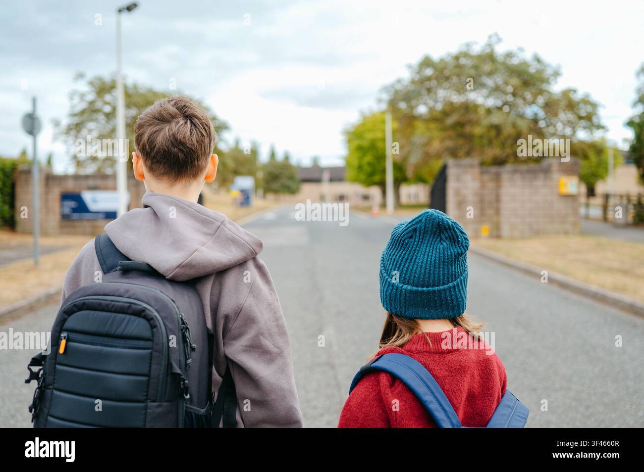 Boy and girl walking toward a school with backpacks Stock Photo