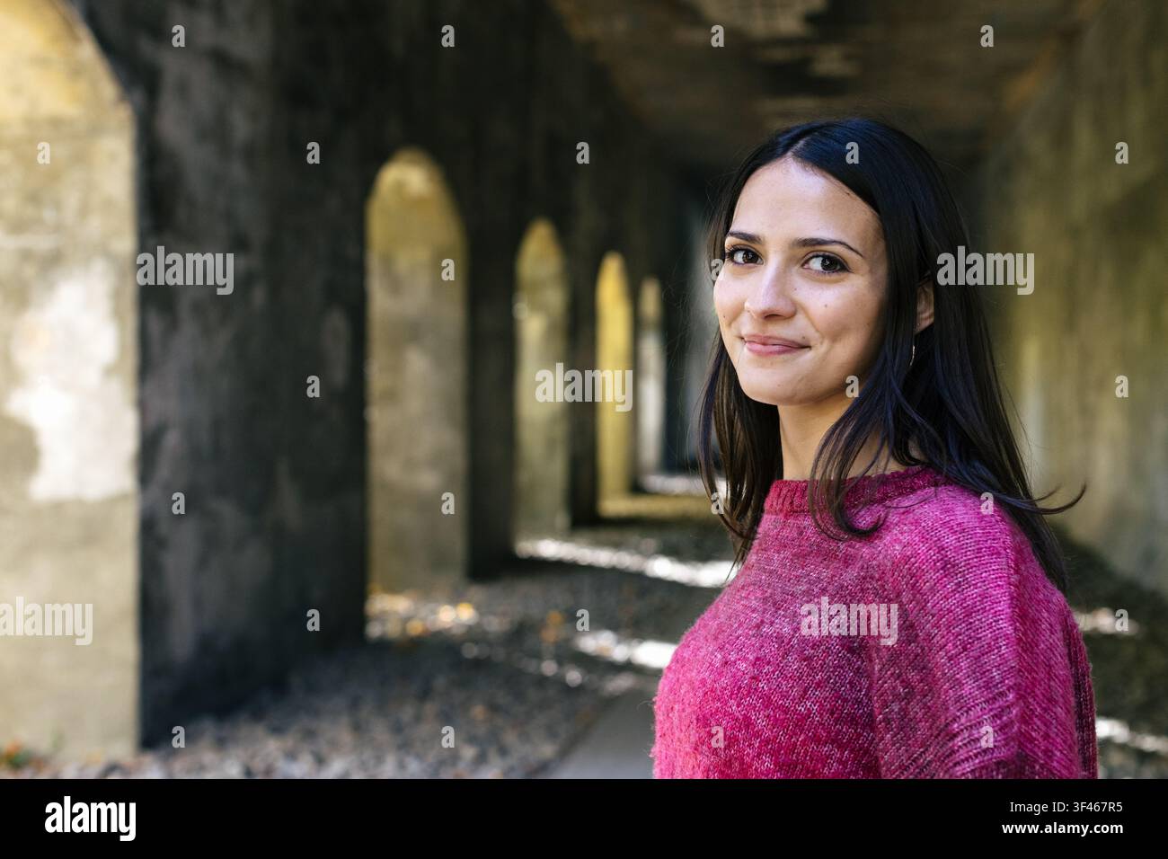 Beautiful young woman smiling in a long stone hallway Stock Photo