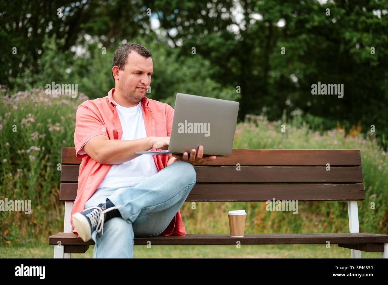 Man working on laptop while sitting on park bench, copy space Stock Photo