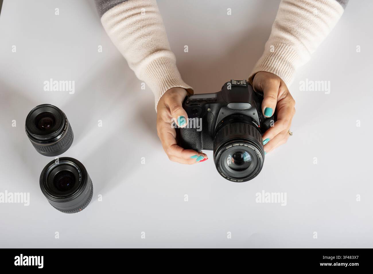 Holding DSLR Camera with Interchangeable Lenses on White Surface Stock Photo