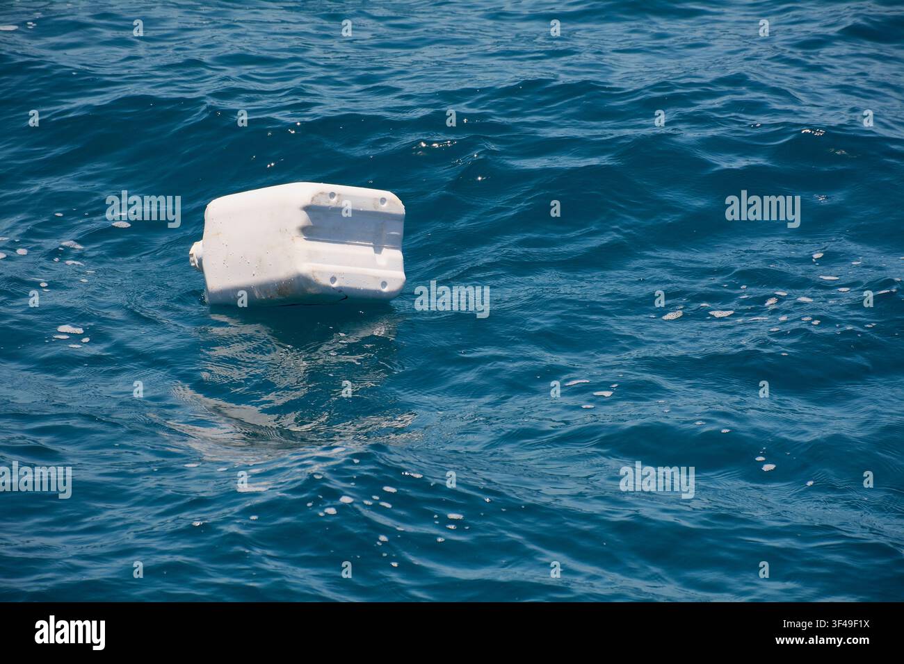 A white plastic container floats on the blue surface of the sea, highlighting issues of marine pollution and plastic waste. Stock Photo