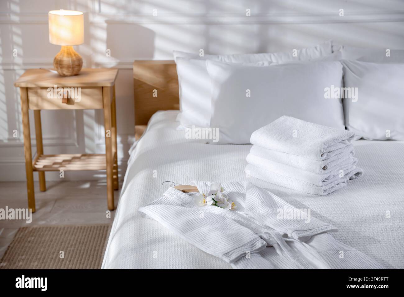 Clean bathrobe, towels and flowers on bed indoors Stock Photo