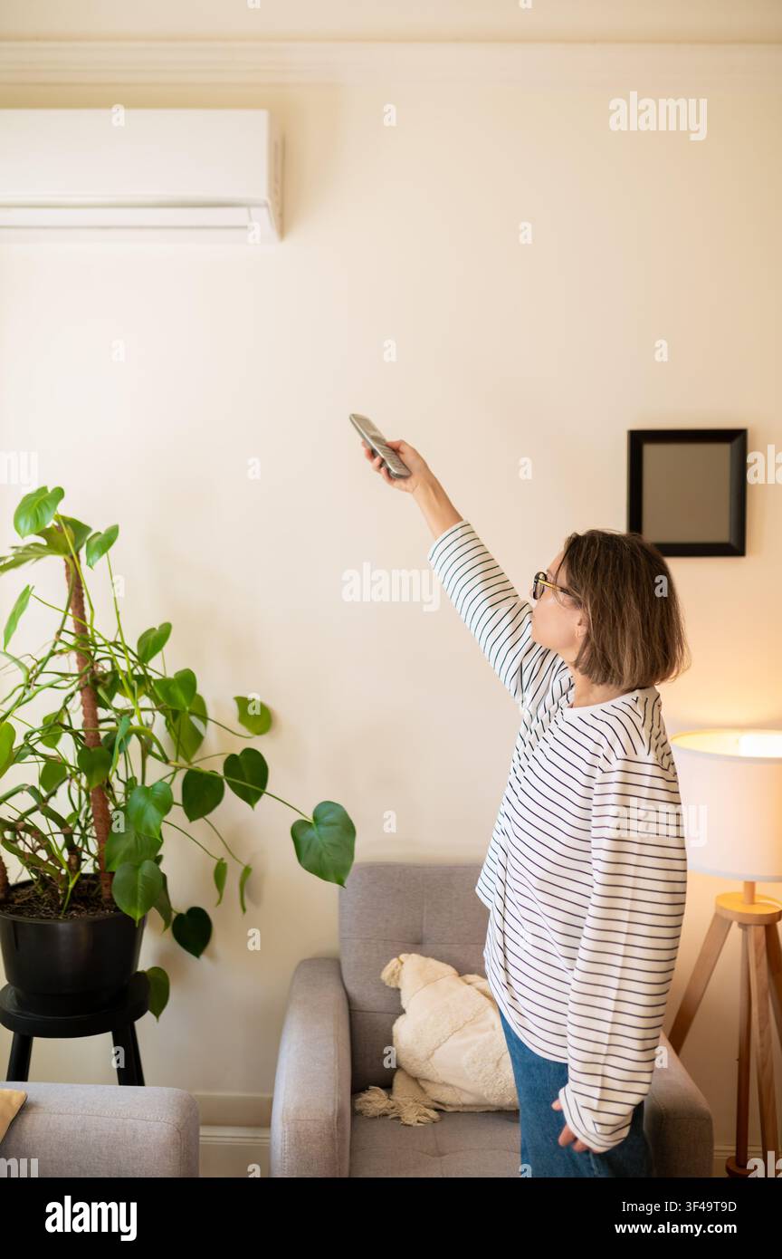 Middle aged woman using air conditioner remote control Stock Photo