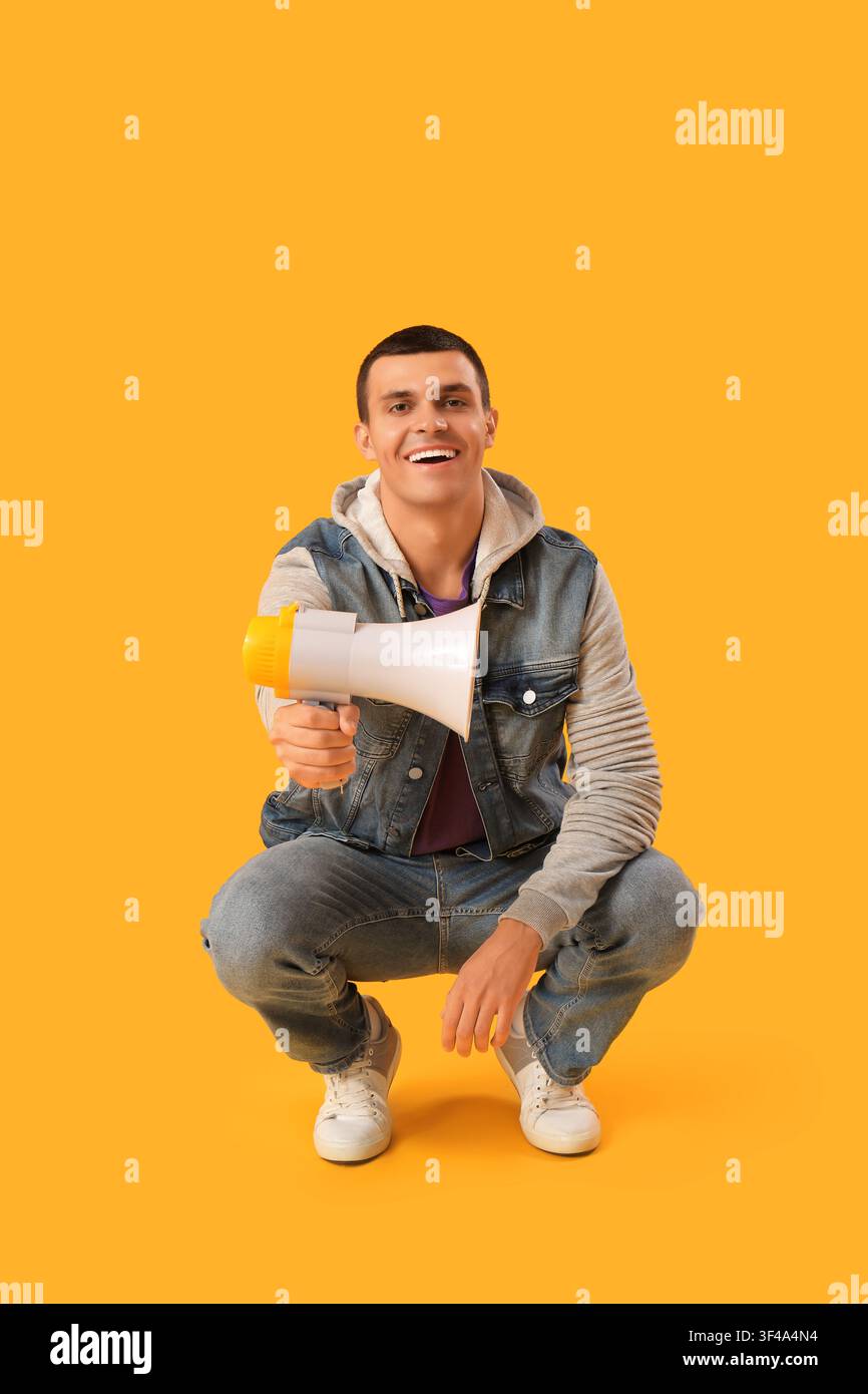 Young man with megaphone on yellow background Stock Photo