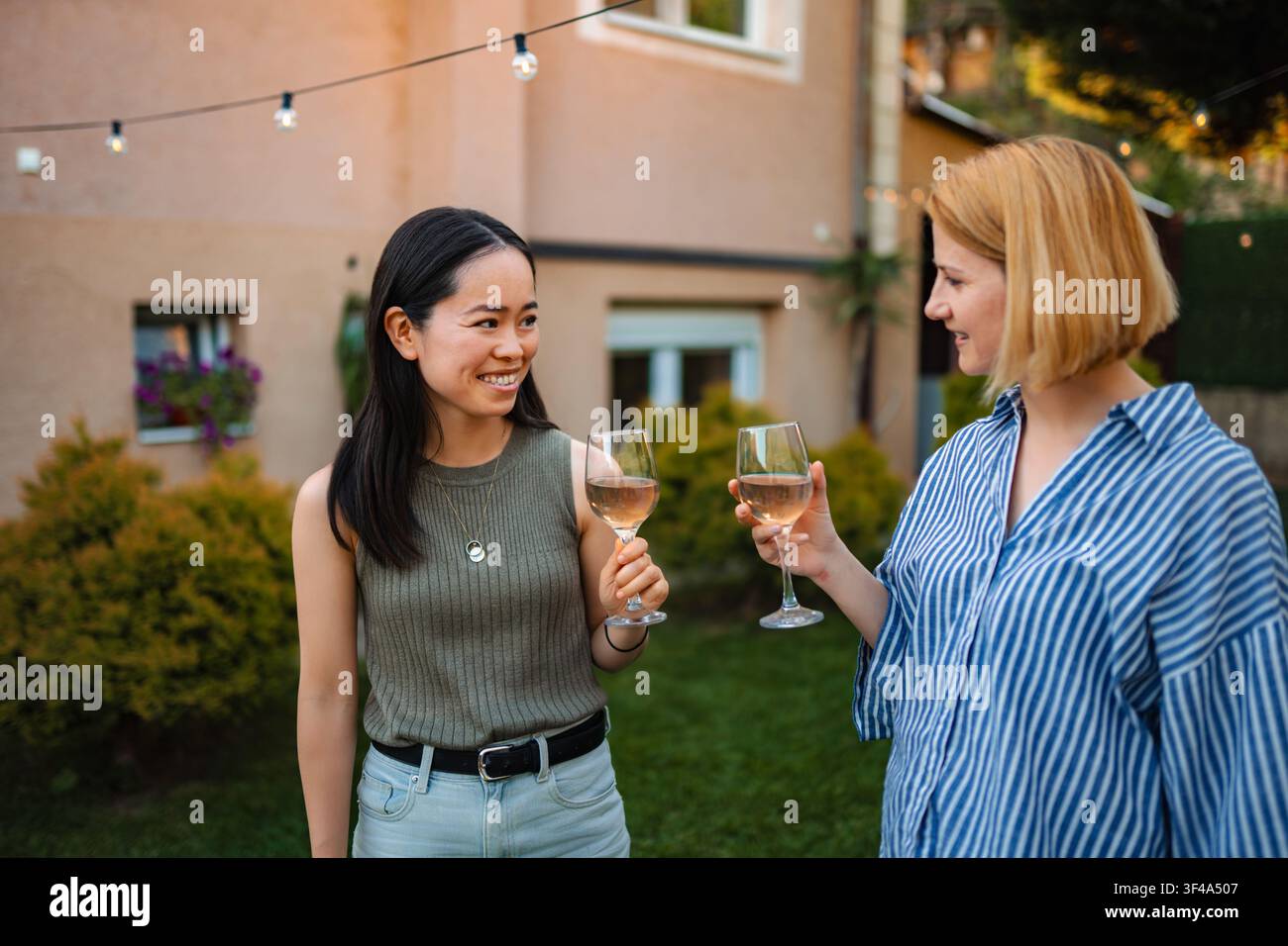 Two happy multi ethnic women toasting rose wine at garden party Stock Photo