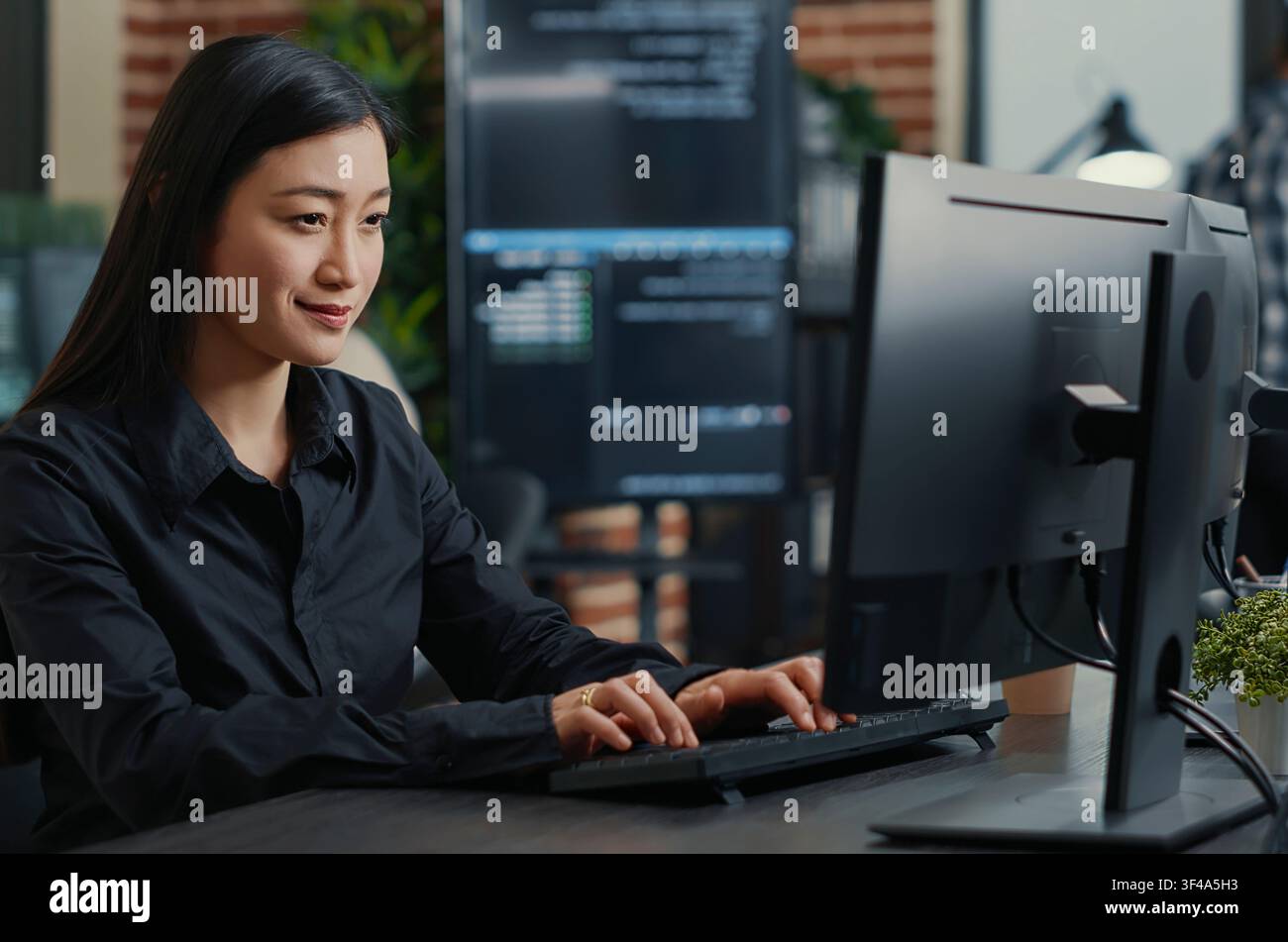 Smiling Asian Programmer Writing Code at Desk at a software development desk after compiling source code successfully, showing algorithm work and coding success. Stock Photo